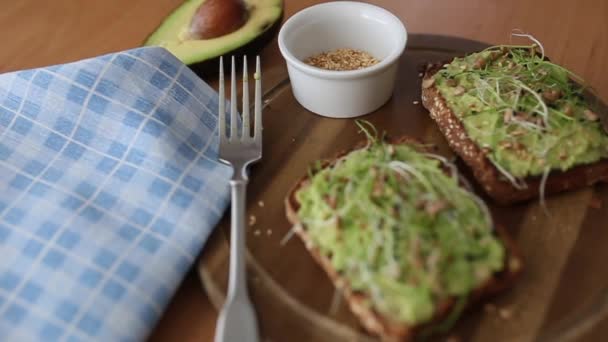 Toast sfocato con microverdi e guacamole in cima. Pane tostato di segale su tavola di legno. Cibo sano a casa. Concetto di cibo vegano. Movimento della fotocamera — Video Stock