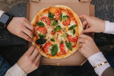 Dışarıdaki kutudan pizza alan çiftlerin en iyi görüntüsü. Erkek ve kadın elleri pizza yiyor. Taze domates fesleğenli vejetaryen pizza ve brokoli. Laktoz ve glütensiz.