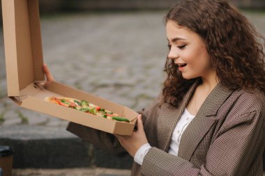 Kadın dışarıda pizza kutusu açıyor. Kadın pizza kutusu açık ve iştah açıcı kokuyor.