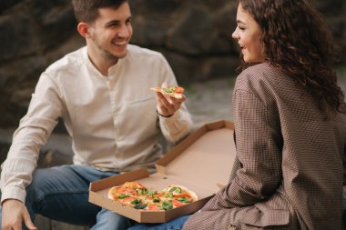 Gülümseyen aşk çifti merdivenlerde vegan pizza yiyor. Yakışıklı adam, kadına bir dilim pizza ver.