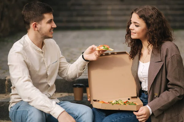 사랑을 나누는 커플 이 계단에서 야채 피자를 먹고 있어. 건방진 남자가 여자한테 피자를 한 조각씩 준다 — 스톡 사진