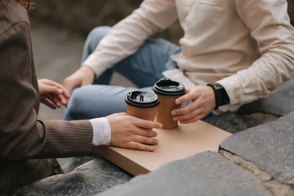 笑顔の愛のカップルは、屋外の階段に座って、コーヒーのカップを保持します。カップルは持ち帰りビーガンピザを持っています — ストック写真