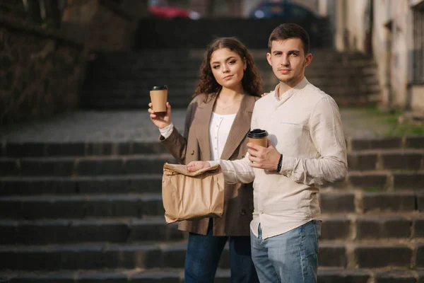 Pareja joven sostiene comida para llevar en las manos y sonríe a la cámara. Espacio para texto — Foto de Stock