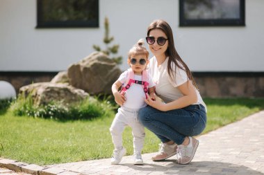 Anne ve sevimli küçük kızı evin önünde yürüyorlar. Mutlu aile dışarıda vakit geçirdi. Anne ve kızı güneş gözlüğü takıyor.