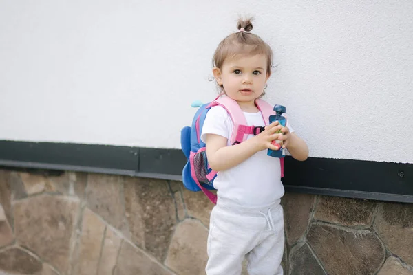 가방을 들고 집 근처를 걷고 있는 귀여운 소녀 — 스톡 사진