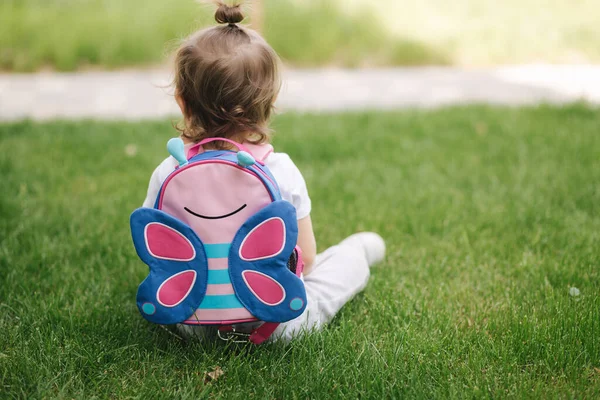 Visszapillantás a kislányra hátizsákkal a szabadban ül a fűben. szóköz a szövegnek — Stock Fotó