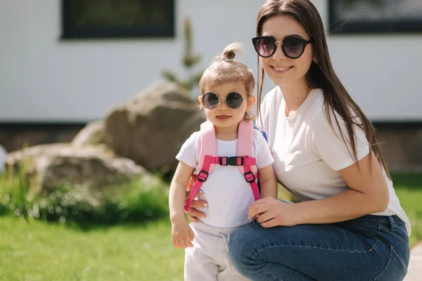 Mamma med sin söta lilla dotter går framför huset. Lycklig familj tillbringade tid utomhus. Mor och dotter i solglasögon — Stockfoto