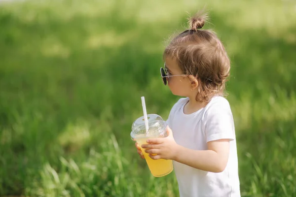 Primo piano di carina bambina in body bianco e occhiali da sole bere limonata all'aperto — Foto Stock