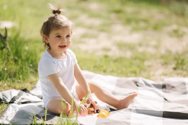 Glückliches kleines Kind sitzt draußen auf Teppich und spielt mit Kuscheltieren. Liebenswertes kleines Mädchen im weißen Body — Stockfoto