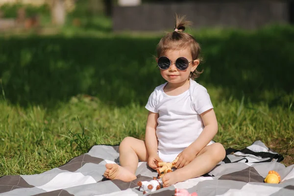 Happy little kid zit buiten op tapijt en spelen met speelgoeddieren. Schattig klein meisje in wit bodysuit — Stockfoto