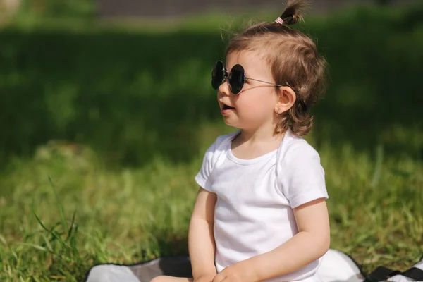 Il bambino felice si siede all'aperto sul tappeto e gioca con gli animali giocattolo. Adorabile bambina in body bianco — Foto Stock