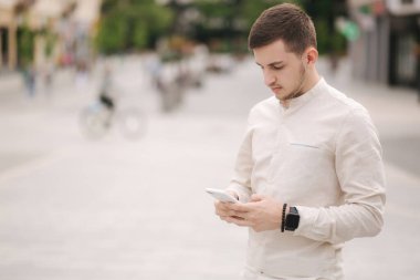 Şehrin merkezinde telefonunu kullanan yakışıklı bir genç adam var. Çevrimiçi oyun oynayan adam dışarıda