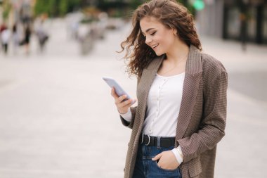 Çekici genç bir kadın şehirde telefon kullanıyor. İnternette, telefonda masaj yazan mutlu bir kadın.