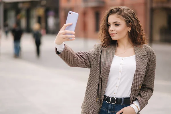 Una joven atractiva usa el teléfono en la ciudad. Feliz hermosa mujer haciendo selfie al aire libre — Foto de Stock