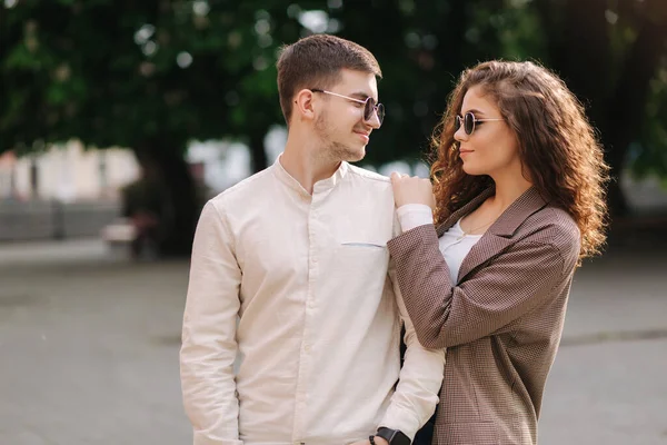 Happy couple walking in the city. Attractive young woman with curly hair and handsome young man in centre of the city. Smiled people in sunglasses outdoors — Stock Photo, Image