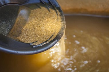 Close up of gold panning pan with sifting sand. Shallow depth of field with focus on sand flowing over edge of pan into water. clipart