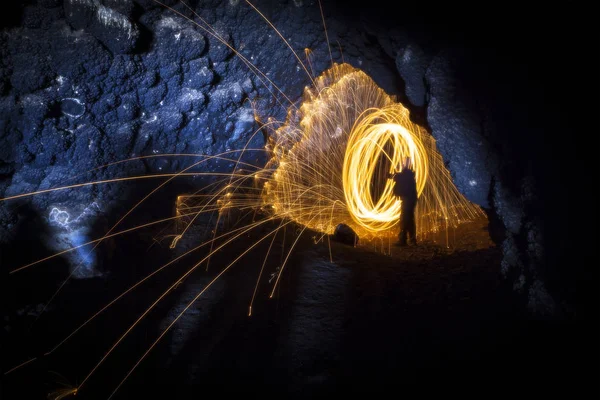 Fire spinning steel wool inside cave with showering sparks