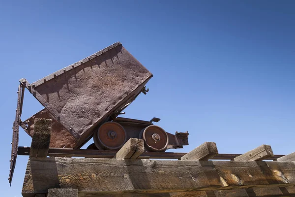Velho carro de minério enferrujado no cavalete sob o céu azul . — Fotografia de Stock