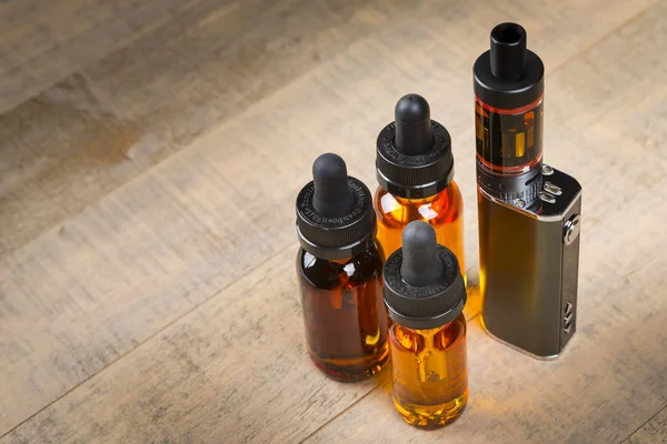 Vaping mod e-cig with tank atomizer and juice bottles over wood background — Stock Photo, Image