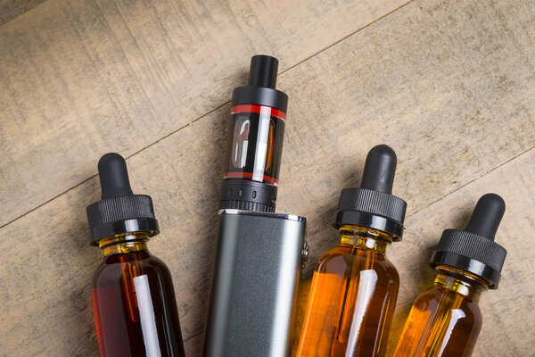 Vaping mod e-cig with tank atomizer and juice bottles over wood background