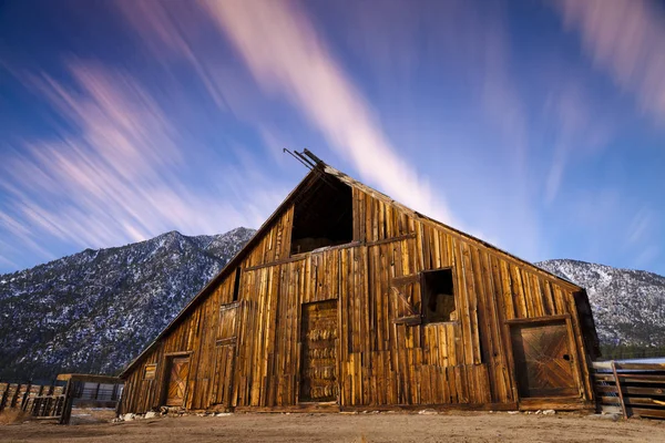 Oude houten schuur bij zonsopgang met strepen van wolken. — Stockfoto