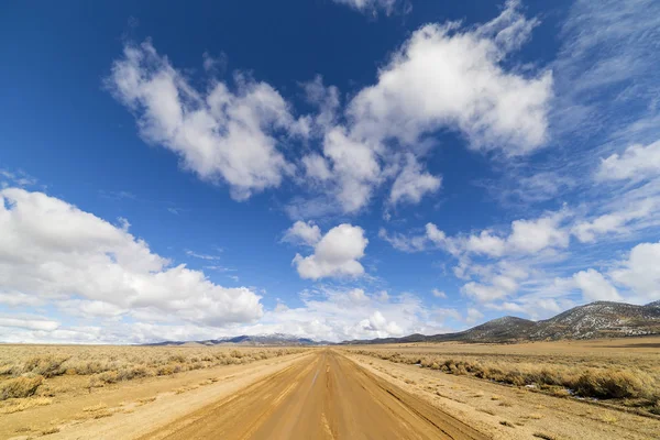Polnej drodze na pustyni Nevada pod błękitne niebo z chmurami. Droga jest mokry brud i błoto. — Zdjęcie stockowe