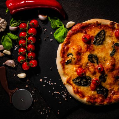 Geleneksel İtalyan pizzası, sebzeler, arka plandaki malzemeler. Pizza fırında pişiyor. Pizza menüsü.