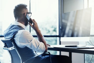 Modern Loft Startup.Creative adam cep telefonu çağrı Partner.Person dijital Tablet masaüstü bilgisayar işyerinde çizim kullanarak çalışma gözlük beyaz gömlek yelek giyen şık sakallı genç adam.