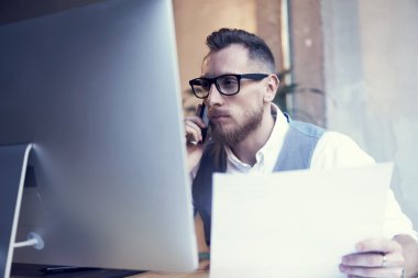Sakallı işadamı Smartphone telefon görüştüğünüz kağıtları Hand.Young masaüstü çalışan beyaz gömlek yelek giyen adam tutarak kullanarak başlangıç iş stratejisi Workplace.Man düşünüyorum.
