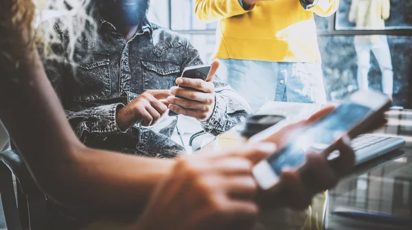 Gros plan de jeunes collègues utilisant des gadgets électroniques dans un bureau ensoleillé. Homme tenant un smartphone ses mains et femme touchant l'écran de son téléphone mobile. Horizontal, flou . — Photo