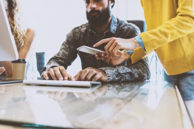 Güneşli bir ofis sürecinde coworking. Ahşap masa, bilgisayarda çalışan adam. Smartphone ekran el sarı kazak giyiyor ve ona dokunan kadın. Yatay görüntü bulanık,.