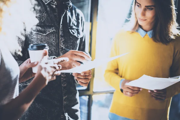 Young team of coworkers making great discussion in sunny office near the window.Man holding a paper in his hands and talking with colleagues.Horizontal, blurred background. — Stock Photo, Image