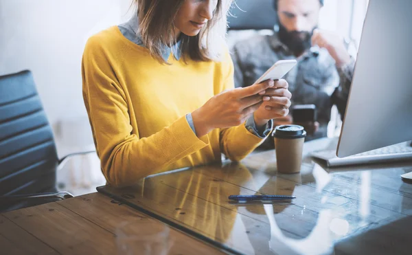 현대 사무실에서 일하고 있습니다. 여성은 핸드폰을 보고 나무 탁자에 앉아 있습니다. 남성 이 스마트폰으로 타이핑하고 있습니다 . Horizontal photo, disred 배경. — 스톡 사진