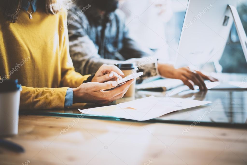 Closeup of young coworkers working with electronic gadgets in sunny office.Man typing on the desktop keyboard and woman using her mobile phone. Horizontal, blurred.