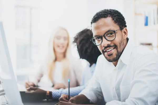 Dunkelhäutiger Unternehmer mit Brille, der in modernen Büros arbeitet.Afrikanischer Amerikaner in weißem Hemd, der in die Kamera blickt und lächelt. Horizontaler, verschwommener Hintergrund — Stockfoto
