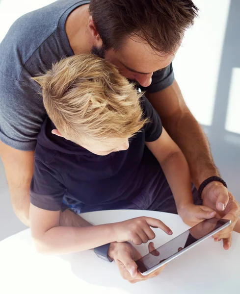 Young boy sitting with father at the table and playing together pc tablet in modern loft. Vertical, blurred background. Top view. — Stock Photo, Image