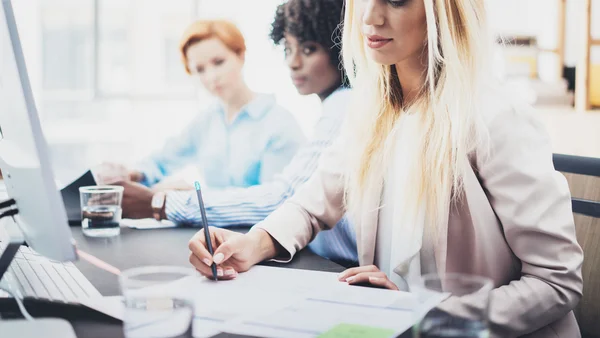 Schöne blonde Frau beim Unterschreiben von Dokumenten am Arbeitsplatz im Büro. Gruppe von weiblichen Mitarbeitern diskutiert gemeinsam Geschäftsprojekt. horizontaler, verschwommener Hintergrund. — Stockfoto