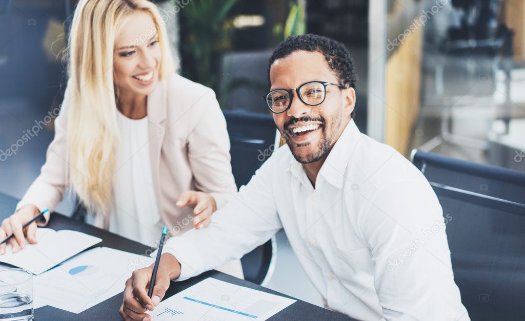 Two young coworkers working together in a modern office.Man wearing glasses, looking at the camera and smiling.Woman discussing with colleague new project.Horizontal,blurred background