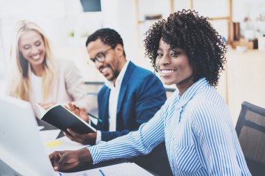 Üç iş arkadaşlarınızla birlikte modern ofis iş projesi üzerinde çalışan grubudur. Gülümseyen, genç çekici Afrikalı kadın ekip çalışması kavramı. Yatay, bulanık arka plan.