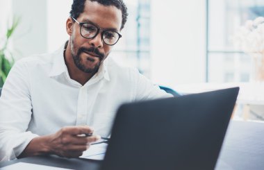 Gözlük takan ve dizüstü bilgisayar kullanma modern office iş arkadaşınız koyu tenli. Afrikalı-Amerikalı adam beyaz gömlekli işyeri üzerinde çalışıyor. Yatay, bulanık arka plan