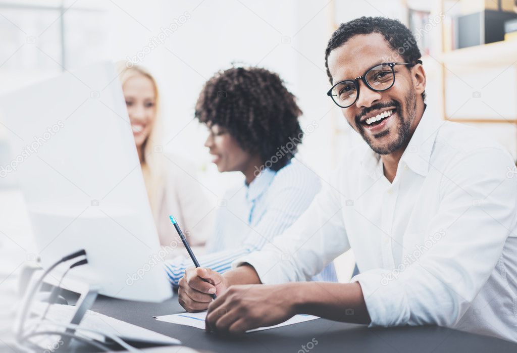 Dark skinned entrepreneur wearing glasses, working in modern office.African american man in white shirt smiling at the camera.Horizontal,blurred background