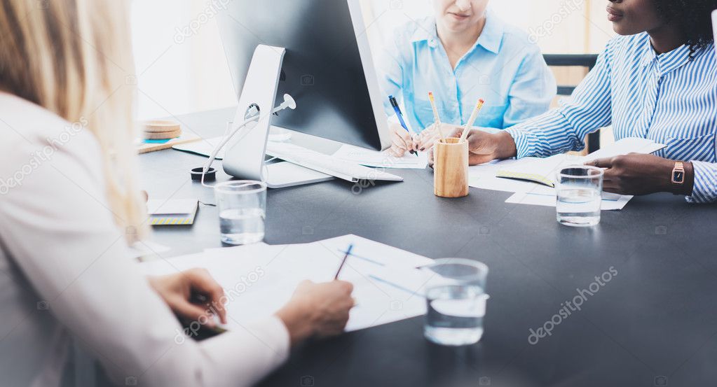 Beautiful blonde woman signing documnet on workplace in modern office. Group of girls coworkers discussing together business ideas. Horizontal, blurred background.