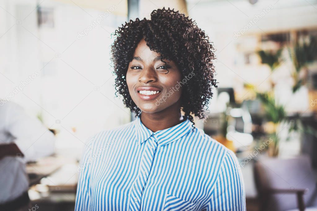 Portrait of pretty african american business woman with afro looking and smiling at the camera.Interior on background in modern office. Horizontal,blurred.