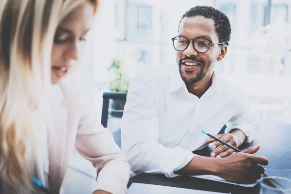 Twee jonge zakenlui samen te werken in een modern kantoor. Zwarte man met bril, kijkend naar de zakenvrouw en glimlachen. Vrouw met collega nieuw project bespreken. Horizontale, wazig . — Stockfoto