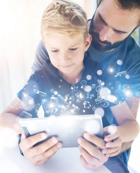 Baba ve küçük oğlu birlikte dinlenme mobil bilgisayarda kapalı oynama. Genç çocuk güneşli evde tablet Pc kullanma sakallı adam. Çocukluk hayalleri simgeler kavramı. Dikey, bulanık arka plan. — Stok fotoğraf
