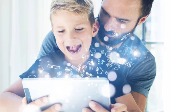 Closeup photo of young boy sitting with father at the table and using pc tablet in modern house.Childhood dreams icons concept.Vertical, blurred background. — Stock Photo, Image