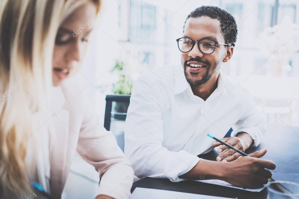 Two young coworkers working together in a modern office.Black man wearing glasses, looking at the businesswoman and smiling.Woman discussing with colleague new project.Horizontal,blurred background