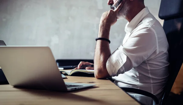 Uomo d'affari adulto barbuto indossare occhiali classici e lavorare al tavolo di legno in soppalco moderno. primo piano orizzontale, sfondo sfocato . — Foto Stock