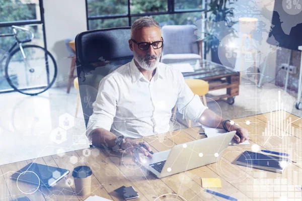 Concepto de pantalla digital con icono virtual, diagrama, gráfico e interfaces. Elegante hombre barbudo de mediana edad utilizando el ordenador portátil en el lugar de trabajo. Fondo horizontal, borroso . — Foto de Stock