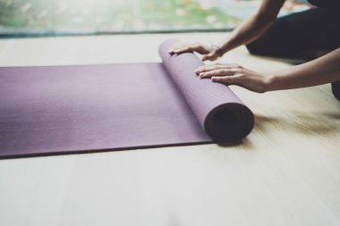 Güzel genç kadın pratik yoga kapalı görünümünü kapatın. Güzel kız paspaslar elle uygulama sınıfı için hazırlanıyor. Sakinlik ve sakin ol, mutluluk kavramı. Yatay, bulanık arka plan.